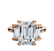 The 18K Rose Gold 3-Stone Baguette Side Stones Set North/South 0.25TCW Engagement Ring features a central diamond with two baguette side stones in a classic prong setting, displayed against a plain white background.