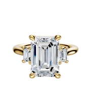 The 18K Yellow Gold 3-Stone Emerald Cut Side Stones 0.25TCW Engagement Ring features a central emerald-cut diamond with two smaller rectangular diamonds on each side, set in classic prongs against a white backdrop.