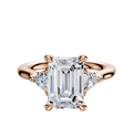 The 18K Rose Gold 3-Stone Engagement Ring features a large center stone with 0.125TCW trillion side stones, shown against a plain white background.