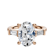The 18K Rose Gold 3-Stone Baguette East/West Side Stones 0.125TCW Engagement Ring features an oval center diamond flanked by two horizontally set baguette side stones on a rose gold band.
