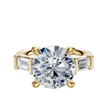 An 18K yellow gold engagement ring featuring a central round diamond accented by two east/west-set baguette side stones (0.25TCW), displayed on a plain white background.