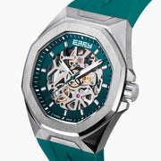 The 42MM Swiss Made Stainless Steel Automatic Skeleton Watch with Diamonds features a teal rubber strap, silver case, partially transparent dial with visible gears, teal bezel and markings, and EBFY branding at the top.