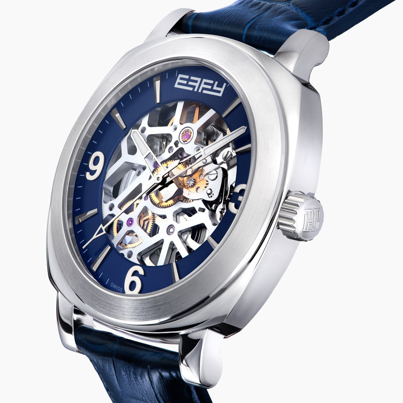 The 41MM Swiss Made Stainless Steel and Leather Automatic Skeleton Watch features a silver case, blue leather strap and bezel, a skeleton dial with visible gears, white hour markers and hands, plus the ERIFY brand name at the top.