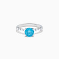 The Lab Grown Blue and White Diamond Ring set in 14K White Gold features a large round blue and white diamond at the center, accented by smaller clear stones, displayed against a white background.