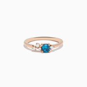 The 14K Rose Gold Blue and White Diamond Ring features a square-cut blue gemstone at the center with small round white diamonds on one side, displayed on a plain white background.