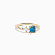The 14K Yellow Gold Blue and White Diamond Ring features a square blue diamond, a smaller square white diamond, and three round white stones set asymmetrically on a plain band.