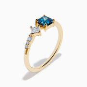 The 14K Yellow Gold Blue and White Diamond Ring features a square blue diamond, a smaller square white diamond, and three round white stones set asymmetrically on a plain band.