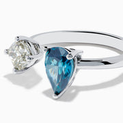 The 14K White Gold Blue and White Diamond Toi Et Moi Ring features a pear-shaped blue diamond and a square white diamond set side by side on an open band, displayed against a white background.
