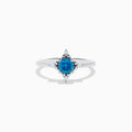 The 14K White Gold Blue and White Diamond Ring features a round blue diamond center with small white stones in a compass pattern, displayed on a white background.