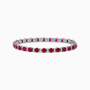 The Ruby Royale 18K White Gold Ruby and Diamond Tennis Bracelet showcases vibrant red rubies in individual prong settings, elegantly displayed against a plain white background.