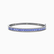 The Nahla Siri 14K White Gold Tanzanite and Diamond Bangle showcases a row of square-cut blue tanzanites between two rows of sparkling diamonds, elegantly displayed against a white backdrop.