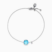 The Ocean Bleu 14K White Gold Blue Topaz and Diamond Bolo Bracelet features a delicate chain, a central round blue topaz, sparkling diamonds, and an adjustable clasp with a small charm near the closure.