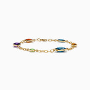 The Mosaic 14K Yellow Gold Multi Gemstone Station Bracelet features five colorful gemstones—blue, green, orange, red, and purple—in various shapes along a gold chain. Shown on a white background, it’s a vibrant accessory for any occasion.