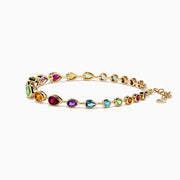 The Mosaic 14K Yellow Gold Bezel Set Multi Gemstone Adjustable Tennis Bracelet (7.0 TCW) features faceted oval gemstones in purple, blue, green, and orange hues with an adjustable clasp, shown on a white background.