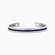 The Men's 925 Sterling Silver and Blue Sapphire Bracelet features a row of blue sapphires at the center and black chevron accents on the edges, offering a bold update to the classic blue sapphire bracelet.