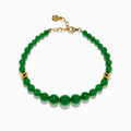 The 14K Yellow Gold Graduated Jade Bracelet features glossy green round jade beads, two 14K yellow gold beads, a gold clasp, and a small gold smiley face charm near the closure.
