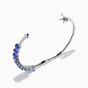 The 14K White Gold Tanzanite and Diamond Bangle features a row of oval-shaped blue tanzanites set in the center, displayed against a white background.