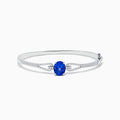 The 14K White Gold Tanzanite and Diamond Bangle showcases a striking round tanzanite centerpiece, accented by rows of sparkling diamonds along the band.
