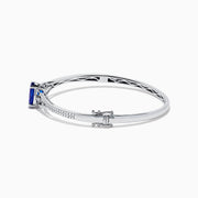 The 14K White Gold Tanzanite and Diamond Bangle showcases a striking round tanzanite centerpiece, accented by rows of sparkling diamonds along the band.
