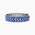 The Nahla Siri Sterling Silver Tanzanite and Diamond Bracelet features three rows of oval-cut tanzanite gemstones in prong settings on an intricate, reflective sterling silver band, displayed against a white background.