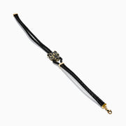 A black braided leather bracelet featuring a signature 14K yellow gold panther center with black diamond and tsavorite accents, finished with a gold clasp for men.