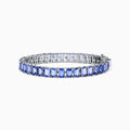 The Nahla Siri Sterling Silver Emerald Cut Tanzanite Tennis Bracelet, featuring a row of individually prong-set gemstones, is elegantly displayed on a plain white background.