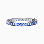 The Nahla Siri Sterling Silver Emerald Cut Tanzanite Tennis Bracelet, featuring a row of individually prong-set gemstones, is elegantly displayed on a plain white background.