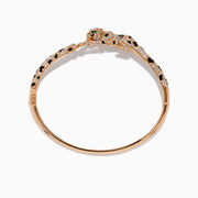 The Signature 14K Rose Gold Diamond and Emerald Panther Bangle features a panther design with its head and tail meeting at the front, adorned with sparkling diamonds and emeralds.