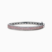 The 14K Two Tone Gold Pink and White Diamond Bangle features an intricate cutout design, accented by a central band with sparkling pink and white diamonds.