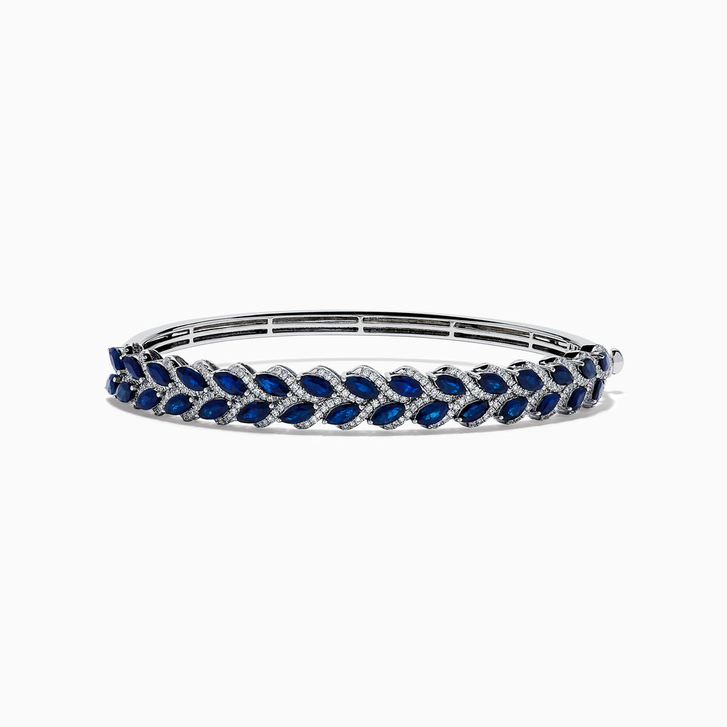 The 14K White Gold Sapphire and Diamond Leaf Motif Bangle features an elegant repeating leaf design with alternating blue sapphires and clear diamonds.