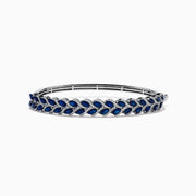 The 14K White Gold Sapphire and Diamond Leaf Motif Bangle features an elegant repeating leaf design with alternating blue sapphires and clear diamonds.