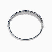 The 14K White Gold Sapphire and Diamond Leaf Motif Bangle features an elegant repeating leaf design with alternating blue sapphires and clear diamonds.
