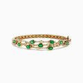 The 14K Yellow Gold Emerald and Diamond Bangle features oval green gemstones, sparkling white diamonds, an elegant openwork design, and a secure clasp.