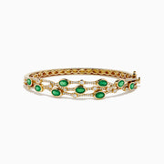 The 14K Yellow Gold Emerald and Diamond Bangle features oval green gemstones, sparkling white diamonds, an elegant openwork design, and a secure clasp.