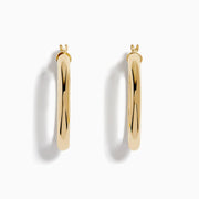 A pair of 14K Yellow Gold Hollow Round Hoop Earrings is shown on a white background, with soft shadows cast to the left.