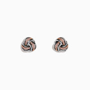 The 14K White Gold Pink Diamond Love Knot Earrings feature an intricate knot design in silver and rose gold tones, accented with sparkling pink diamonds. They are displayed against a plain white background.