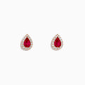 A pair of 14K rose gold ruby and diamond pear halo stud earrings with red rubies framed by diamonds, shown on a white background.