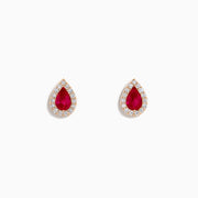A pair of 14K rose gold ruby and diamond pear halo stud earrings with red rubies framed by diamonds, shown on a white background.