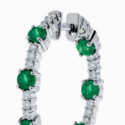The 14K White Gold Emerald and Diamond Hoops showcase alternating round emeralds and diamonds in silver hoops, displayed against a white background.