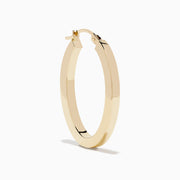 A pair of 14K Yellow Gold Square Tube Oval Hoop Earrings displayed vertically on a white background, casting soft shadows to the right.