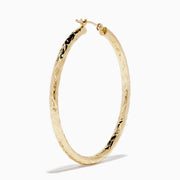 A pair of 14K Yellow Gold Crystal Cut Tube Hoops, large and textured, are displayed vertically on a white background with soft shadows beneath each earring.
