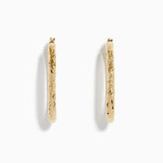 The 14K Yellow Gold Crystal Cut Tube Oval Hoops feature a textured, engraved floral pattern and delicate crystal cut detailing, shown against a plain white background.