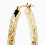 The 14K Yellow Gold Crystal Cut Tube Oval Hoops feature a textured, engraved floral pattern and delicate crystal cut detailing, shown against a plain white background.