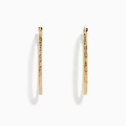 A pair of 14K Yellow Gold Oval Tube Baguette Cut Hoop Earrings, thin and textured, are displayed vertically with clasps at the top against a plain white background.