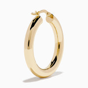The 14K Yellow Gold Tube Hoop Earrings are shown vertically on a plain white background, with soft shadows cast to the left.