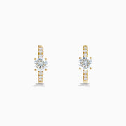 The Lab Grown Diamond Round Huggie Earrings in 14K Yellow Gold feature a central round lab diamond accented by a row of smaller lab diamonds, all set in sleek yellow gold and displayed on a white background.