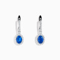 Introducing the 14K White Gold Oval Blue Sapphire and Diamond Drop Earrings, featuring striking oval blue sapphires surrounded by sparkling diamonds in a vertical drop design, set in elegant 14K white gold with diamond-accented hooks.