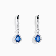The 14K White Gold Pear Shape Blue Sapphire and Diamond Drop Earrings feature teardrop-shaped sapphires surrounded by white diamonds, set in elegant white gold, shown on a white background.