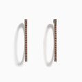 The 14K Rose Gold Brown Diamond 1.5 Inch Hoop Earrings, featuring slim vertical hoops with dark brown diamonds, are photographed against a plain white background, casting soft oval-shaped shadows to the left.