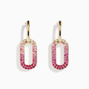 The 14K Yellow Gold Pink Sapphire and Diamond Earrings feature gold hoops with oval pendants, encrusted in a gradient of white diamonds to deep pink sapphires, crafted in 14K yellow gold and shown on a white background.